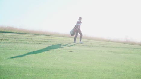 golfer on golf course carrying bag with clubs in idyllic setting, on hill