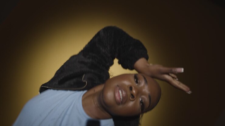 Head And Shoulders Studio Portrait Shot Of Young Woman Dancing In Spotlight Against Yellow Background 7