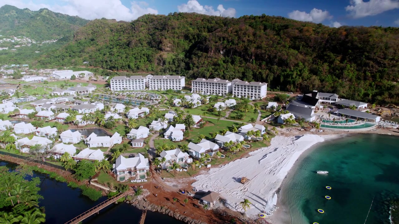 Quét drone ở độ cao lớn qua một khu nghỉ dưỡng sang trọng ở Caribe. Góc nhìn ghi lại các cụm biệt thự, hồ bơi, bãi biển cát trắng và kiến trúc khu nghỉ dưỡng nổi bật trên nền núi non xanh tươi