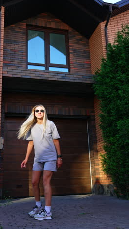 Woman in casual outfit near modern home. A woman with long hair stands outside a brick house, enjoying the warm sunlight while looking playful and relaxed
