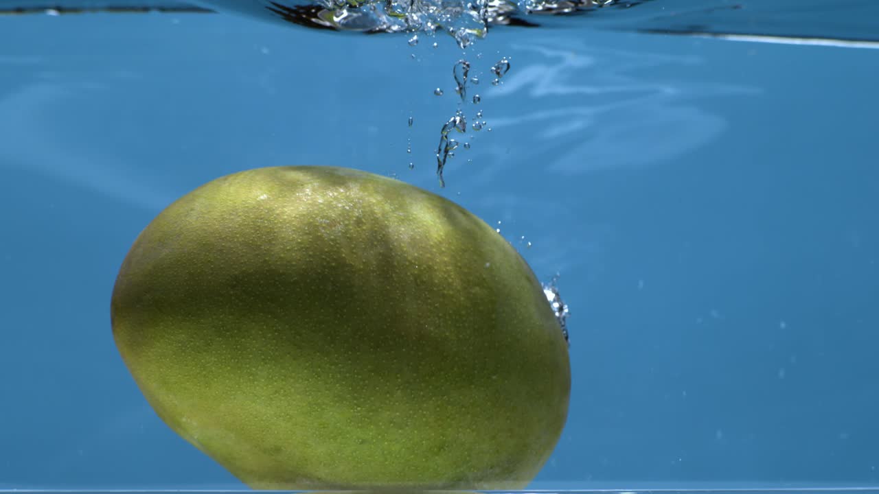 mango cayendo en el agua en cámara súper lenta con fondo azul