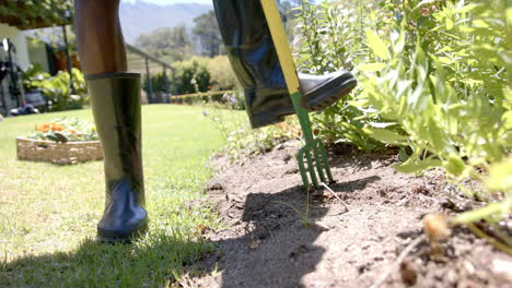 gardening, person in rubber boots using garden fork in backyard garden