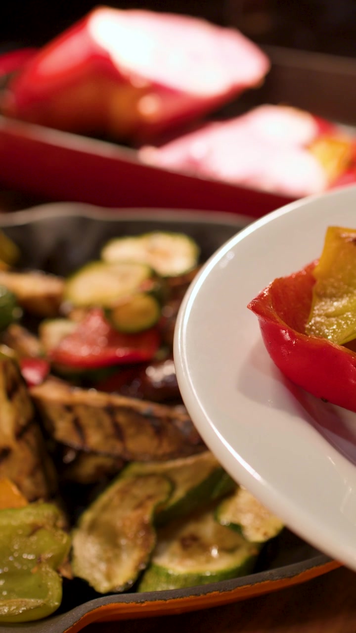 Pinze di metallo posizionano zucchine e peperoni grigliati su un piatto bianco a un buffet.