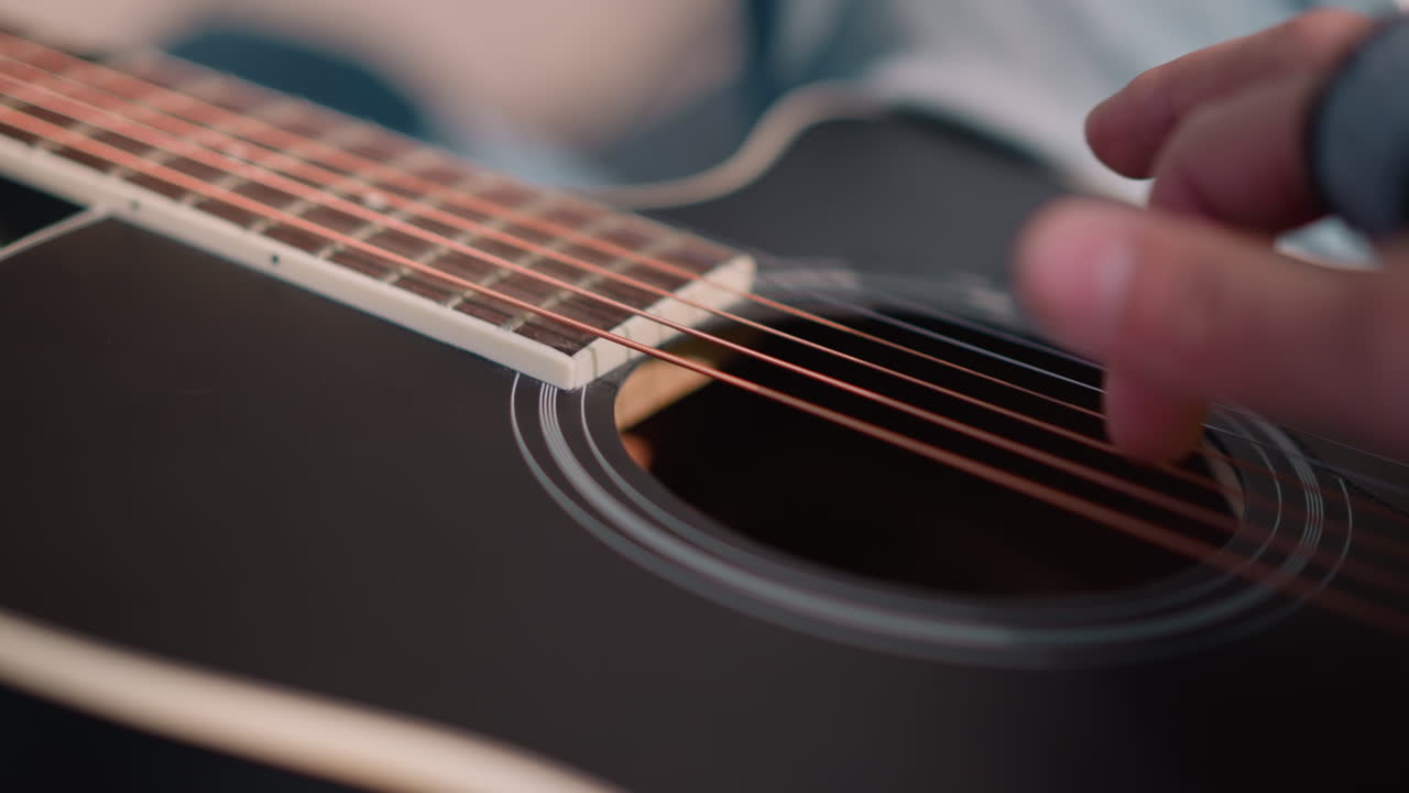 closeup acoustic guitar string detail gentle finger picking on black gloss body, light blue sleeve visible, soft natural lighting, warm timbre and subtle resonance, studio practice vibe, focused