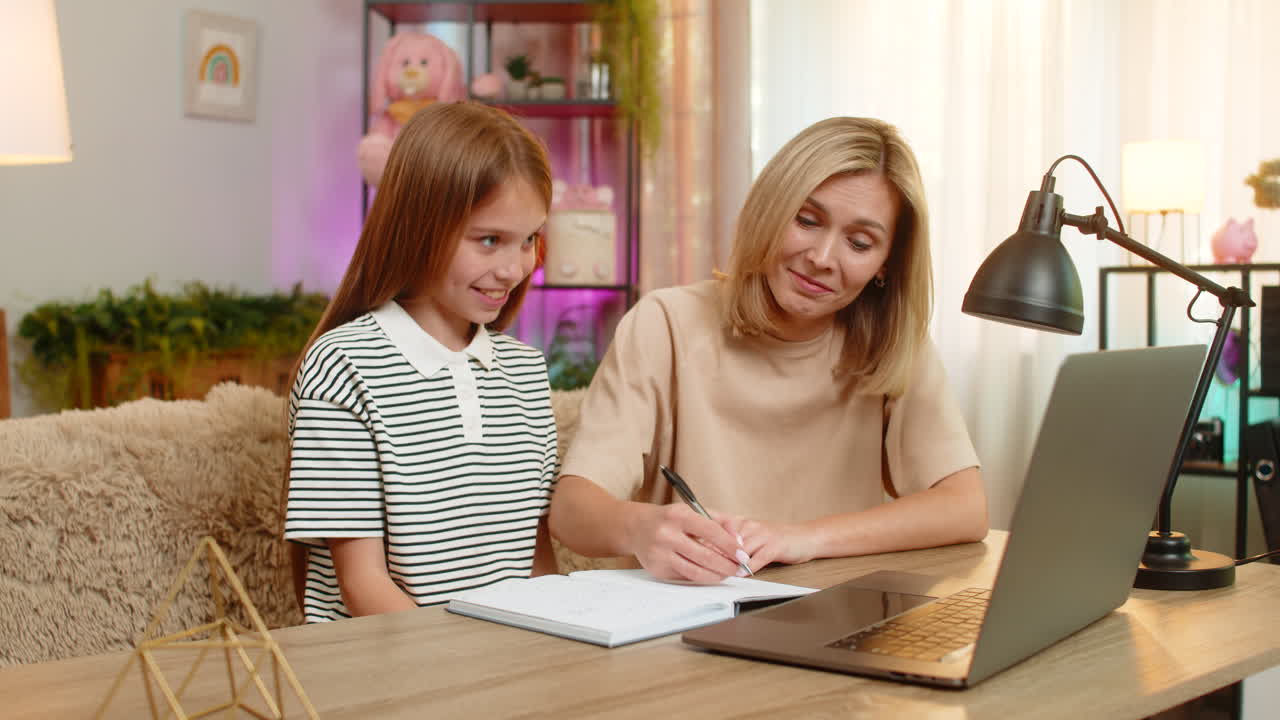 Bambina bambina con la madre che studia a casa sul divano e fa appunti per i compiti a casa nel quaderno scolastico