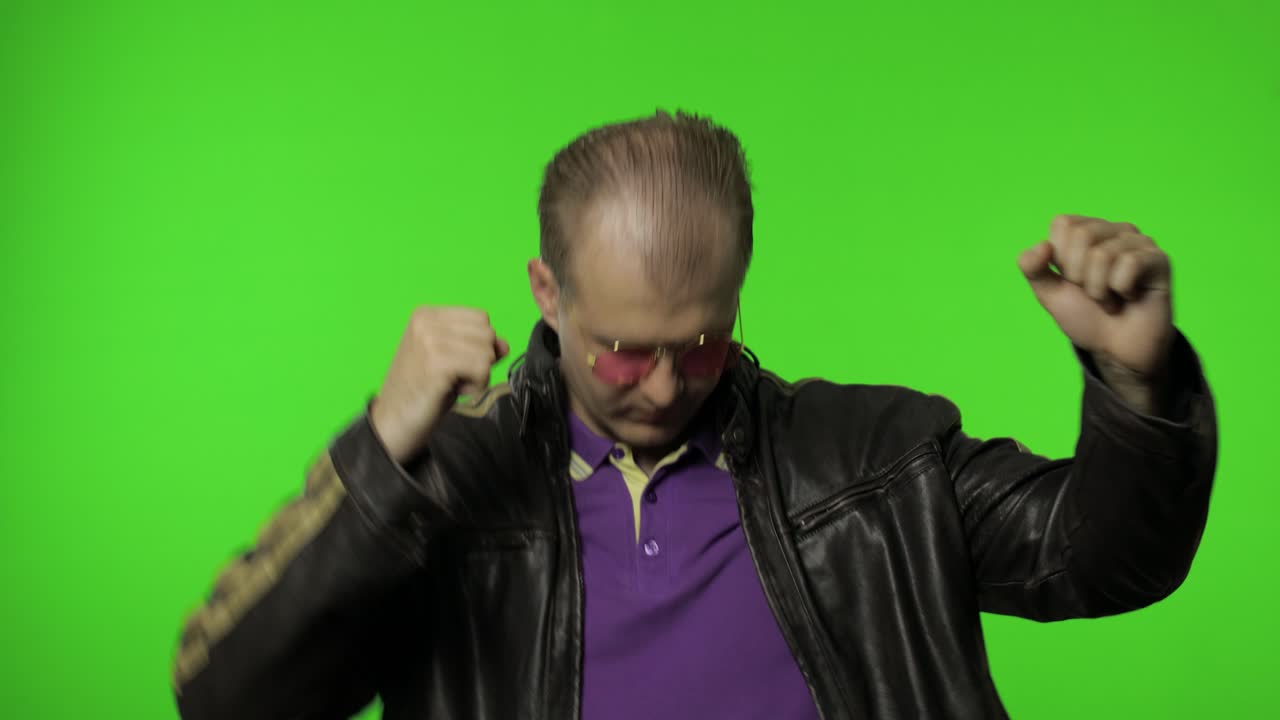 hombre rockero juguetón con gafas de sol rosas moviéndose en danza, sonriendo, haciendo posturas de dab, gesto de éxito
