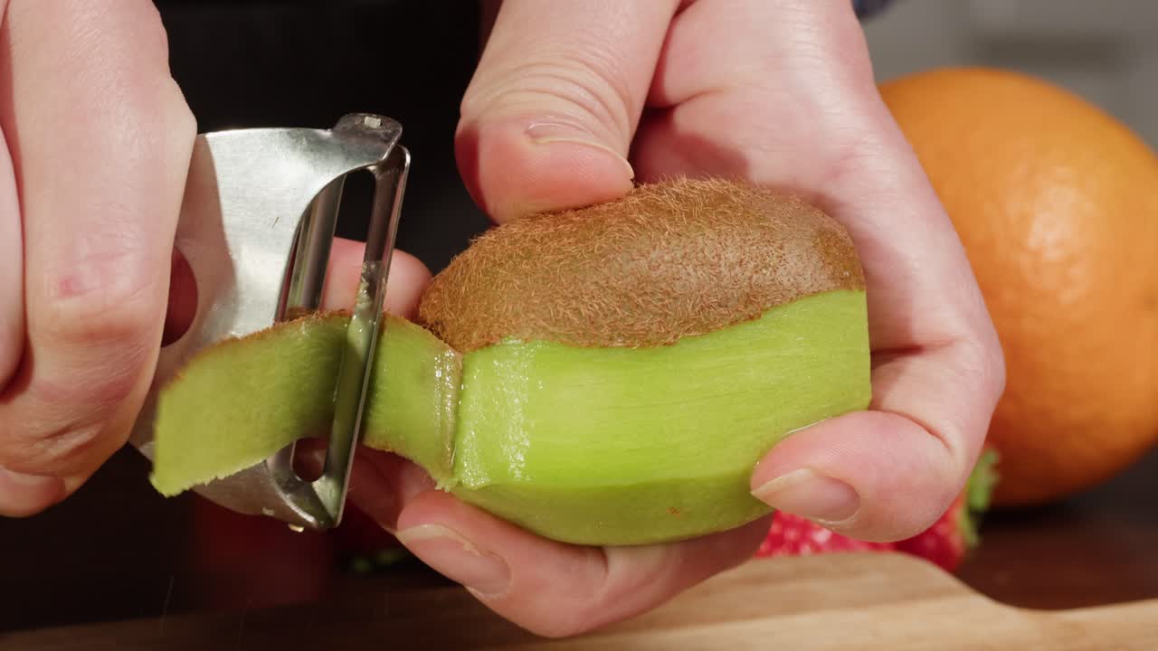 Close Up of Hands Peeling a Fresh Kiwi Fruit with a Peeler