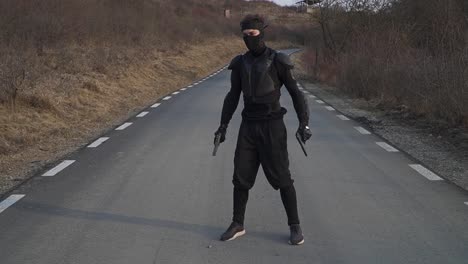 dynamic image of a stealth ninja striking a martial arts pose on a deserted road surrounded by dry vegetation. perfect for action ads, film, and creative projects.