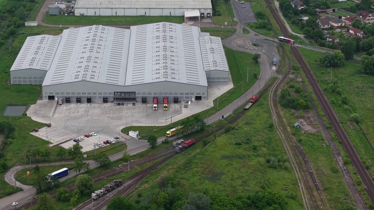 Una prospettiva aerea mostra un grande magazzino industriale e una fabbrica d'acciaio in Ungheria, evidenziando l'integrazione della logistica ferroviaria e stradale.