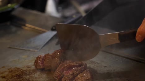 close-up of a chef using a spatula to sear meat on a hot griddle.