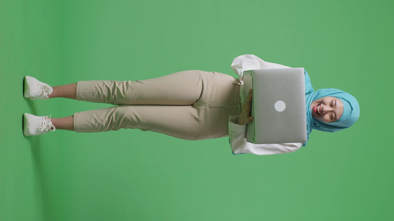 cuerpo lleno de mujer musulmana asiática mirando una computadora portátil luego gritando gol celebrando mientras estaba de pie en la pantalla verde estudio de fondo