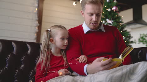 vista inferior de padre e hija sentados en el sofá cerca del árbol de navidad