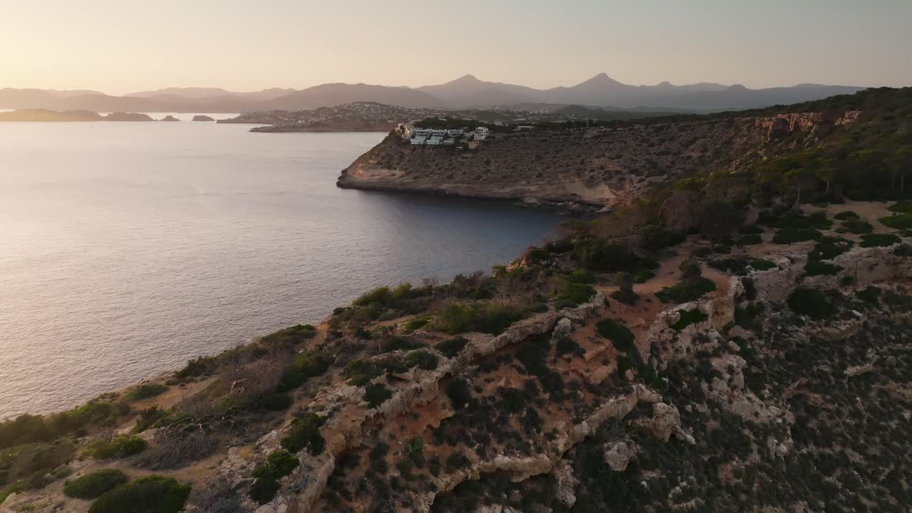 Aerial - coastal limestone cliff near calm bay during golden hour, Mallorca