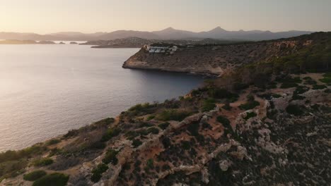 Aerial---coastal-limestone-cliff-near-calm-bay-during-golden-hour,-Mallorca