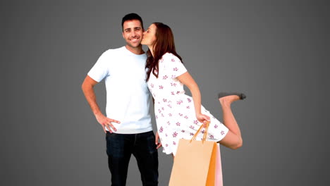 man being kissed on his cheek by his girlfriend on grey background