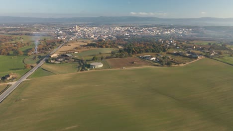 Luftvideo-Eines-Neu-Gesäten-Feldes-Mit-Einer-Unbefestigten-Straße-In-Der-Mitte-Und-Bergen-Im-Hintergrund-Grünes-Kultiviertes-Feld-Von-Llagostera-Gerona