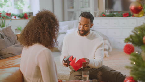 Loving-Couple-Drinking-Champagne-And-Opening-Gifts-Around-Christmas-Tree-At-Home