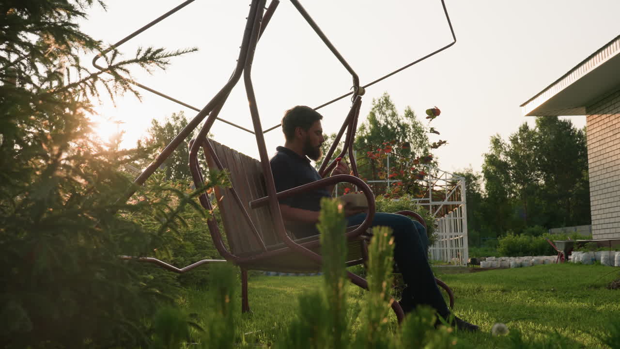 golden sun rays cast warm glow on farmer seated on swing bench eating freshly harvested strawberries from garden box in serene orchard setting surrounded by lush greenery under calm afternoon sky