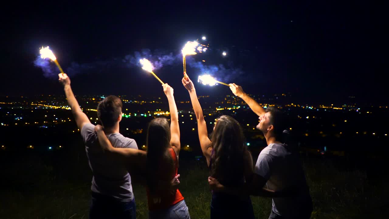 4명의 사람들이 도시 배경에 불꽃놀이 막대기를 들고 있다.