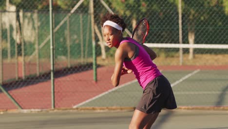 Video-of-focused-african-american-female-tennis-player-holding-racket-and-hitting-ball