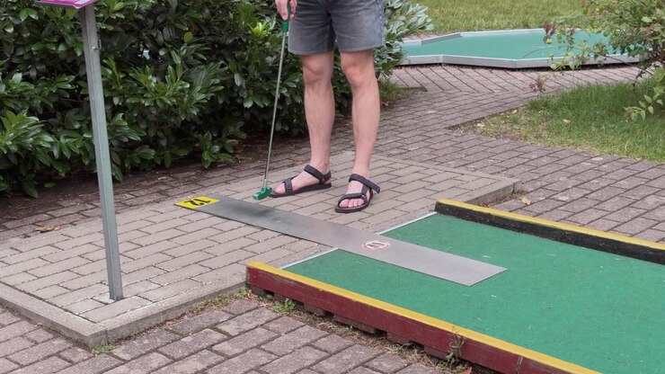 Uomo che gioca a mini-golf all'aperto, che si prepara a colpire la palla sul putting green.