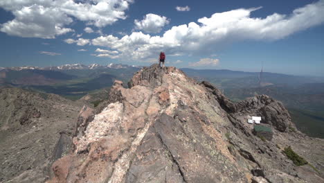 female hiker with a backpack walking on top of peak under clouds on sunny summer day with amazing view of landscape