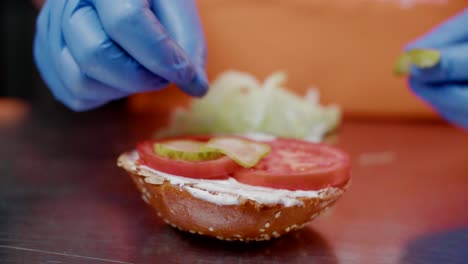 vegetables are placed on burger bun in fast food kitchen, close-up