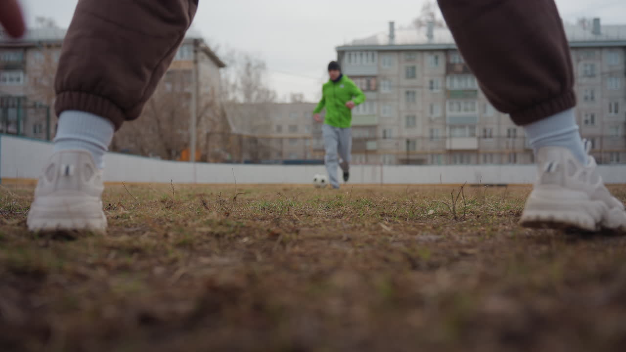 enfrentamiento en un campo sucio, paisaje urbano con acción deportiva intensa, jugador desafiado por un defensor sobre una superficie de juego mojada, escena deportiva urbana que revela un momento tenso entre jugador y oponente