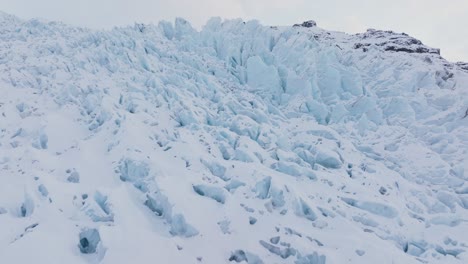 Aerial-panoramic-landscape-view-over-ice-formations-in-Falljokull-glacier-covered-in-snow,-Iceland,-during-sunset