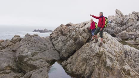 pareja de excursionistas mayores con mochilas apuntando hacia una dirección mientras están de pie en las rocas