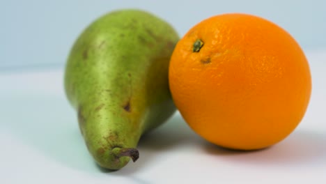 pera verde grande fresca, naranja jugosa gira lentamente sobre un fondo azul claro, concepto de comida saludable, primer plano extremo, cámara gira a la izquierda