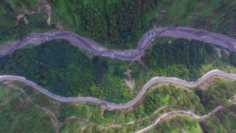 aerial flight over the car driving along the road surrounded by forest, a curved winding roads trough the forest with river, top down shot of traffic on roads through the spring forest