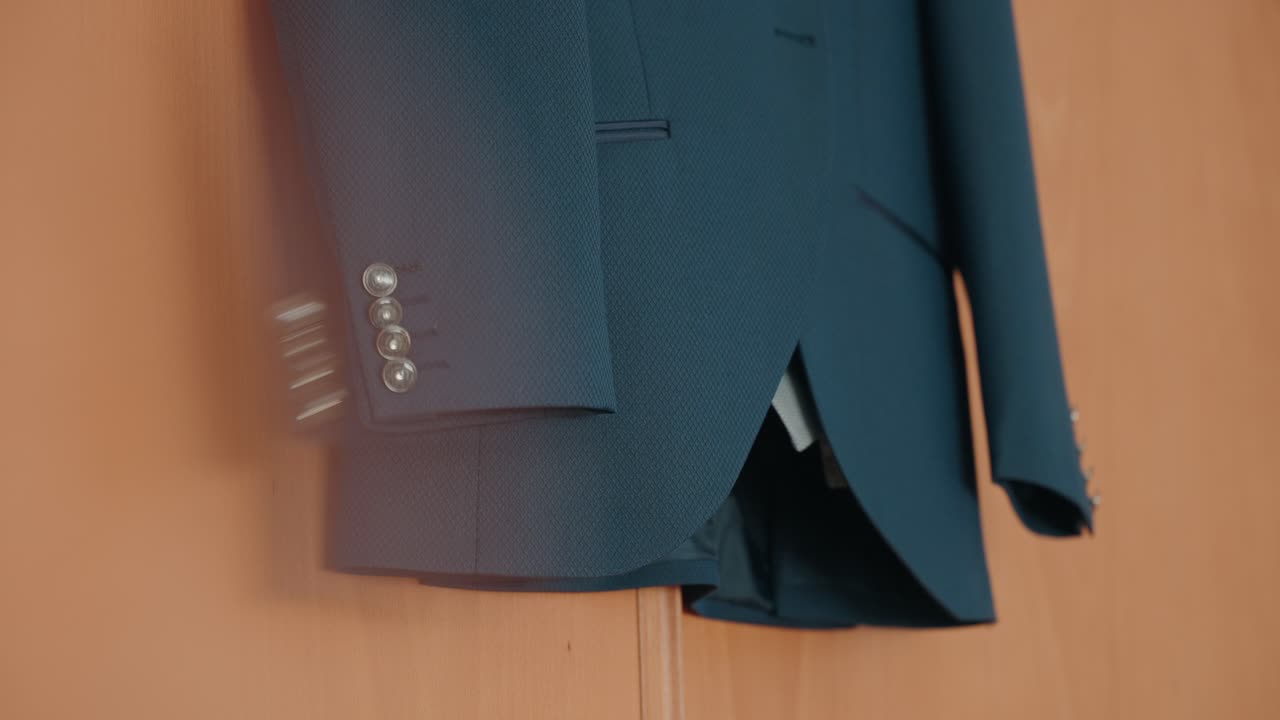 Chaqueta de traje azul colgada en interior mostrando los botones de la manga y el tejido