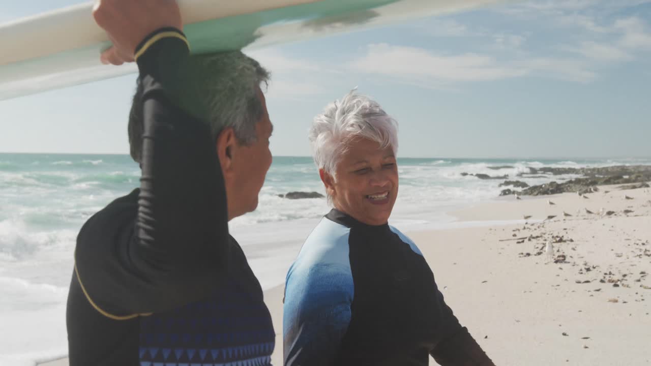 perfil de una feliz pareja hispana senior caminando por la playa con una tabla de surf