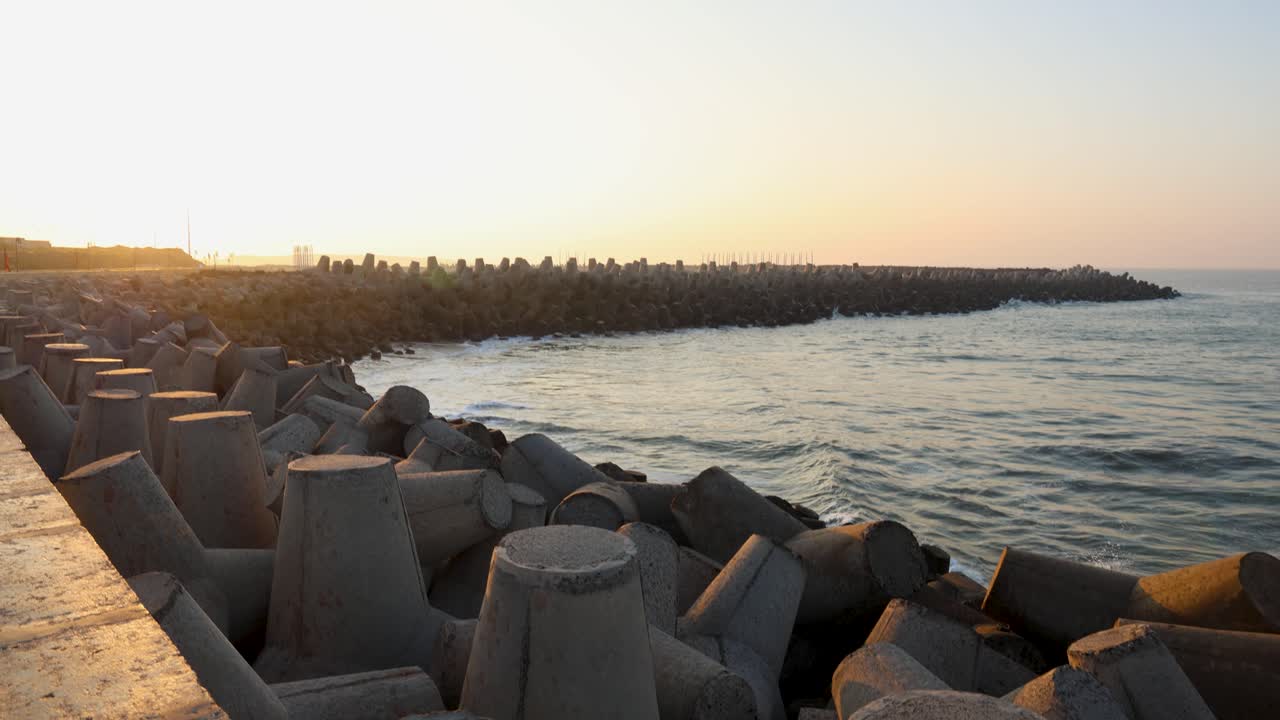 coastal sea waves hitting concrete tetrapod breakwater during sunset along shoreline