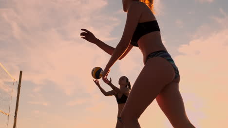 SLOW-MOTION-LOW-ANGLE-CLOSE-UP-SUN-FLARE:-Athletic-girl-playing-beach-volleyball-jumps-in-the-air-and-strikes-the-ball-over-the-net-on-a-beautiful-summer-evening.-Caucasian-woman-score-a-point.