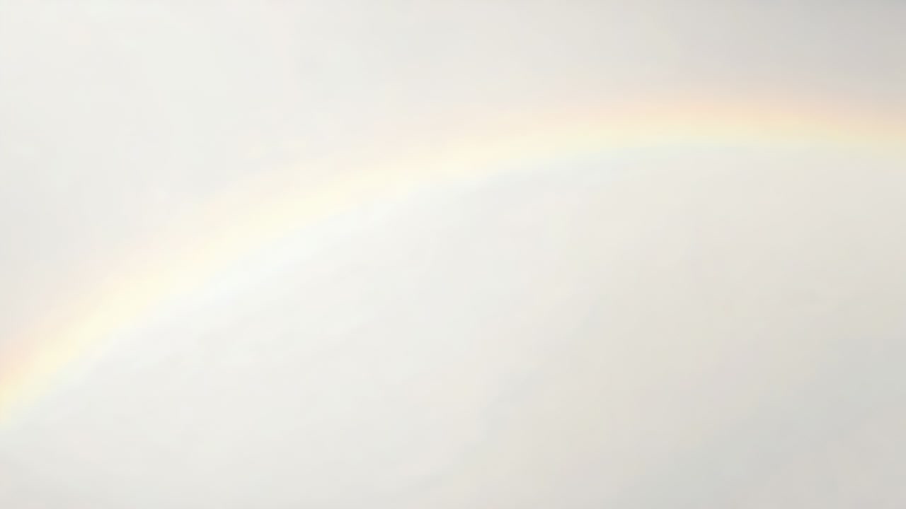 Un debole arco iride appare e si illumina attraverso il cielo nuvoloso dopo una schiarita, rivelando fasce pastello.