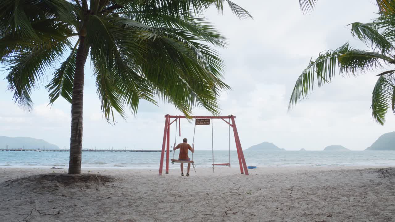 Turista maschio che si gode un'altalena sulla spiaggia di An Hai sull'isola di Con Dao, Vietnam