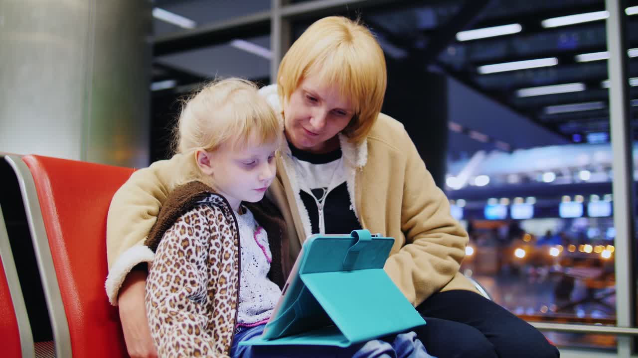 madre e hija esperando su vuelo niña jugando en una tableta