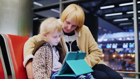 madre e hija esperando su vuelo niña jugando en una tableta