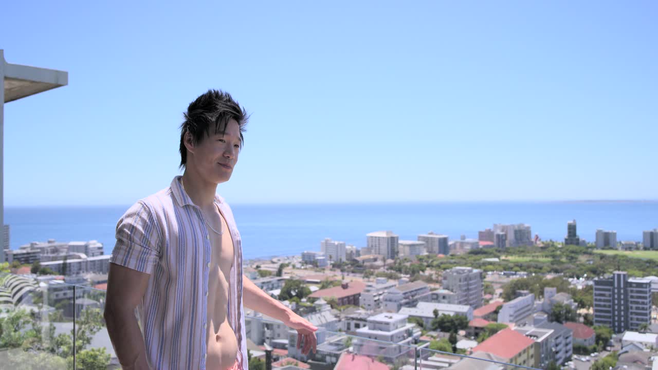 バルコニーの手すりに寄りかかり、微笑みながら身を乗り出し、海から安らぎを得ている成人アジア人男性。コピースペースあり。