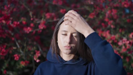 Woman-chew-gum-and-touch-hair,-sunny-outdoor-park-with-Chinese-Quince-shrub