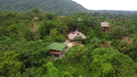 Drone-flies-over-the-lush-forest-to-house-closeup-shows-roof,-wooden-wall,-window-and-stairs,-Santa-Marta,-Columbia