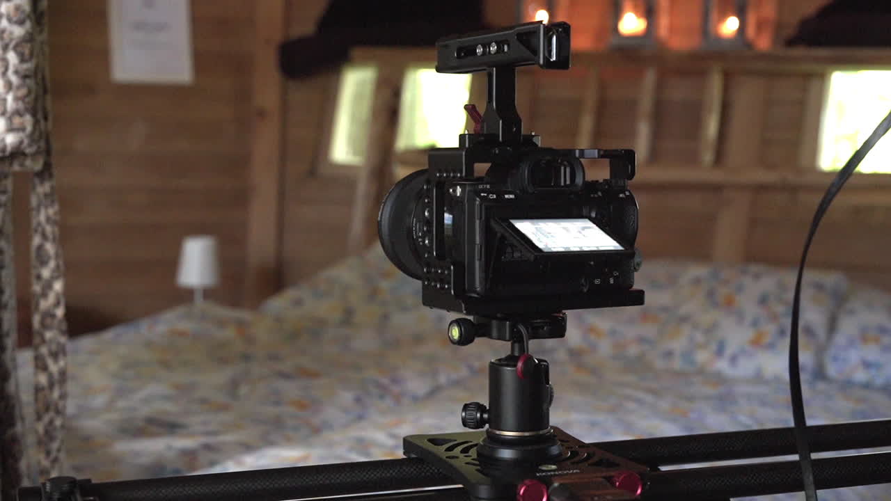 tiro de rastreamento de uma câmera deslizante movendo-se lentamente em um rack e gravando um vídeo de um grande quarto rústico de madeira com uma cama grande coberta com lençóis antiquados