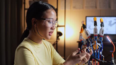 close up of teen asian girl holding and looking at the circuit board while repairing a cyborg hand at home