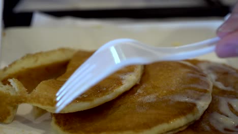 close up of child's hand with knife and fork. the child is cutting pancake.