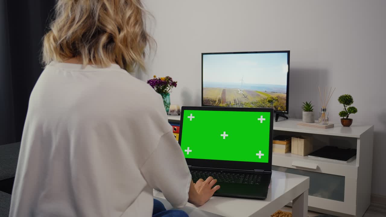 una mujer caucásica hace una búsqueda web en una computadora portátil con pantalla verde y tecla de croma.