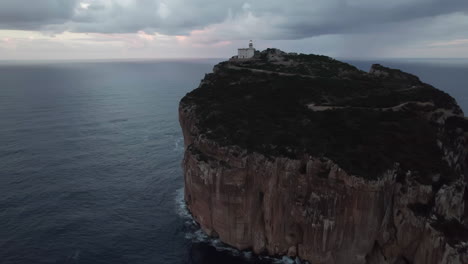 Cape-Caccia,-Sardinia:-aerial-view-in-orbit-of-the-illuminated-lighthouse-of-this-famous-cape-and-during-sunset