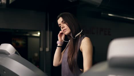 Atractiva-Joven-Deportista-Con-Pelo-Largo-Y-Moreno-Poniéndose-Auriculares-Inalámbricos-Y-Empezando-A-Correr-En-La-Cinta.-Metraje-En-Interiores.-Estilo-De-Vida-Saludable,-Fitness,-Bienestar.