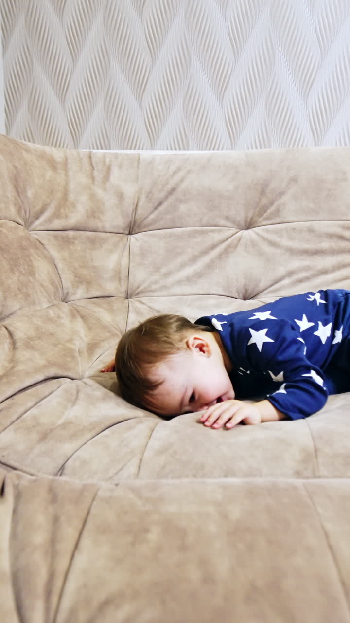 Active Caucasian kid crawls by the big sofa. Baby wearing blue clothes having fun at home. Vertical video